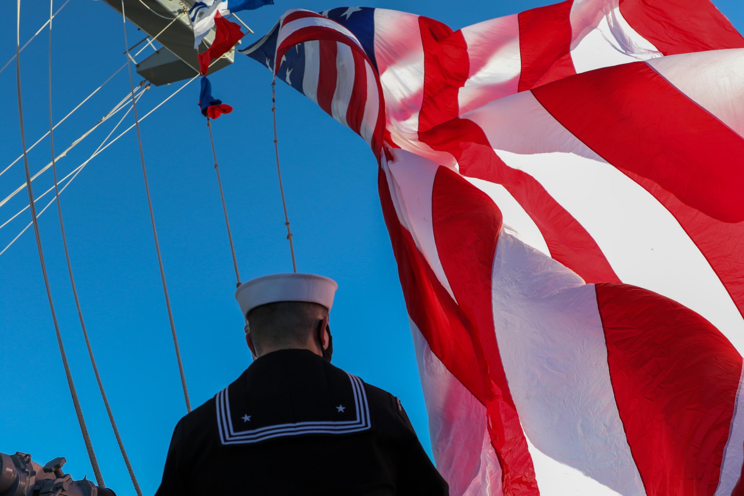 Quartermaster 2nd Class Steven Pettit hoists the ensign on the mast aboard the aircraft carrier USS Abraham Lincoln (CVN 72). (U.S. Navy photo by Mass Communication Specialist Seaman Michael J. Cintron) 220103-N-MC925-1076