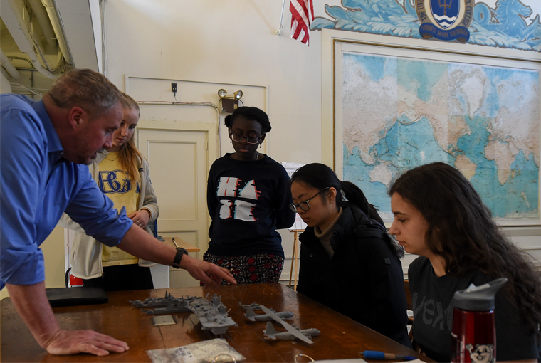 Photo of Tony Fox, an associate professor at U.S. Naval War College, explaining the capabilities of different aircraft and ships to students from Massachusetts Institute of Technology.